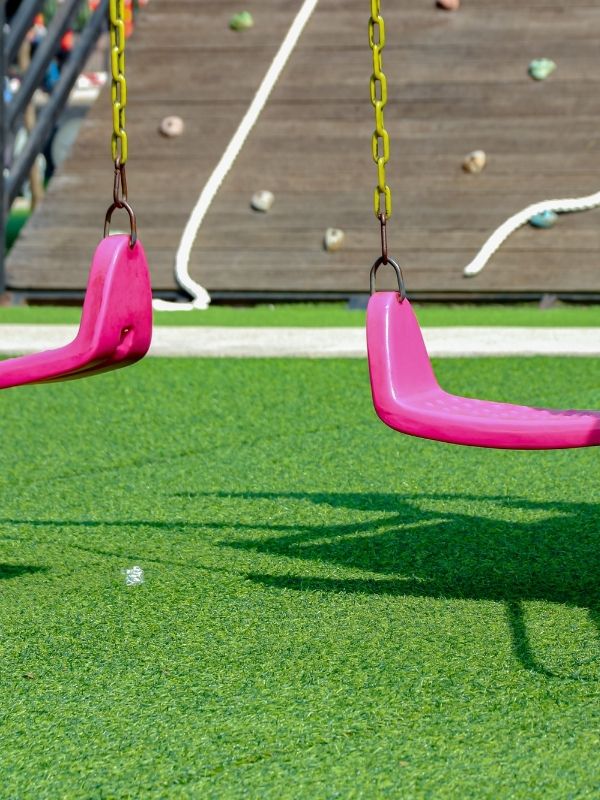 A set of swings over artificial turf. 